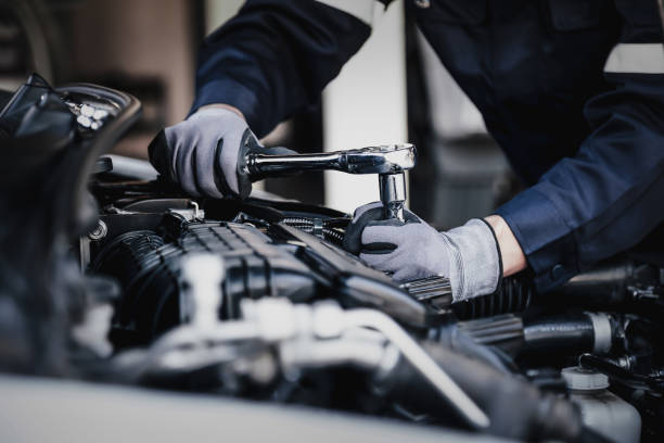 Une personne travaille sur un moteur de voiture, probablement dans un garage ou un atelier. La scène met en scène des éléments automobiles tels qu'une pièce et des vêtements de mécanicien.